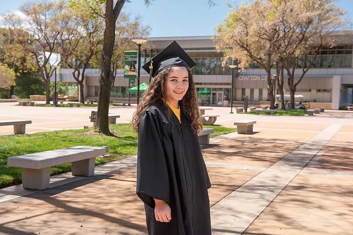 11-year-old, Alisa Perales, is Crafton Hills College’s youngest graduate smiling at Crafton Hills College building